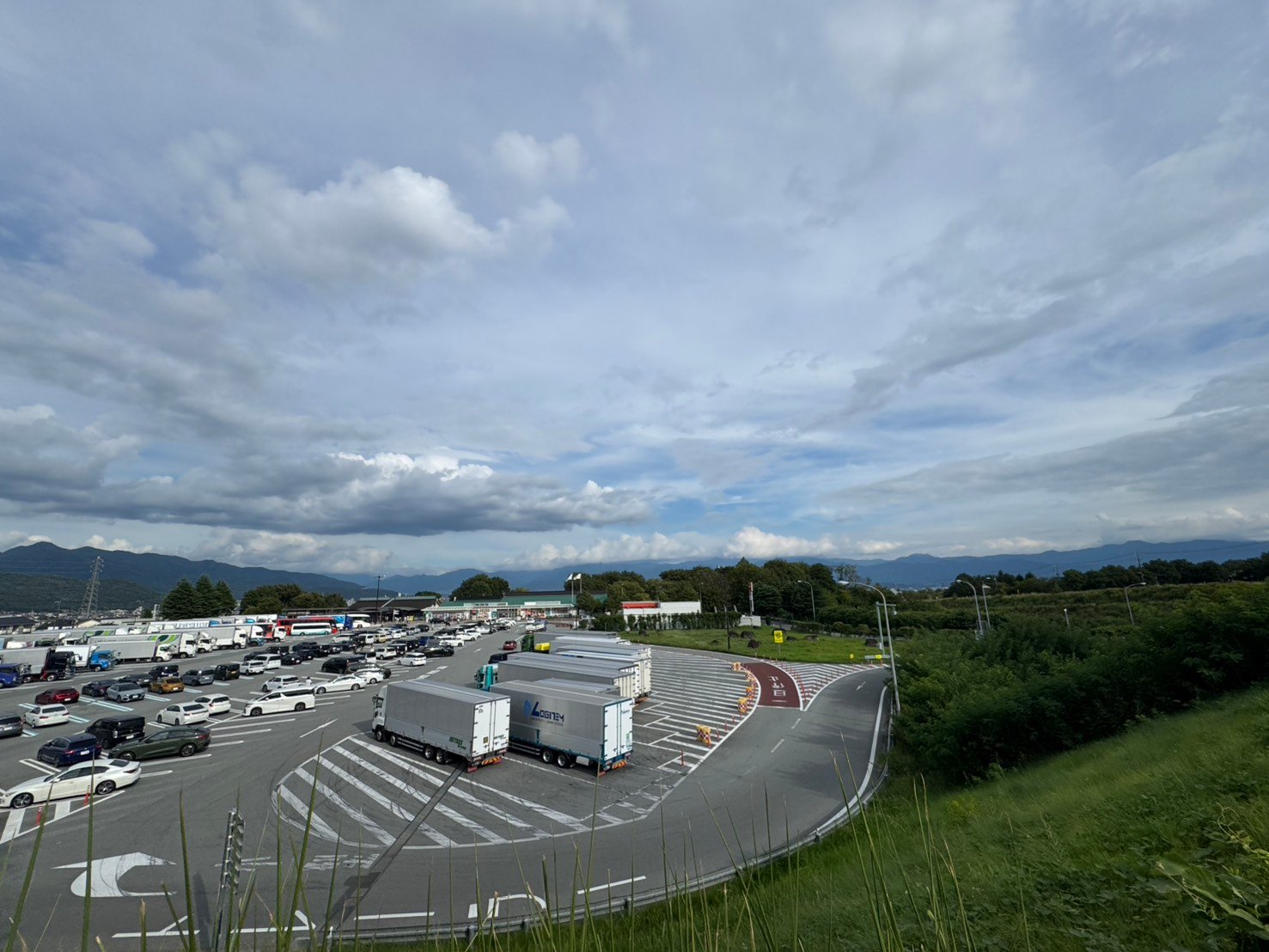 山並みを背景に乗用車と大型トラックが並ぶ双葉SA下りの駐車場