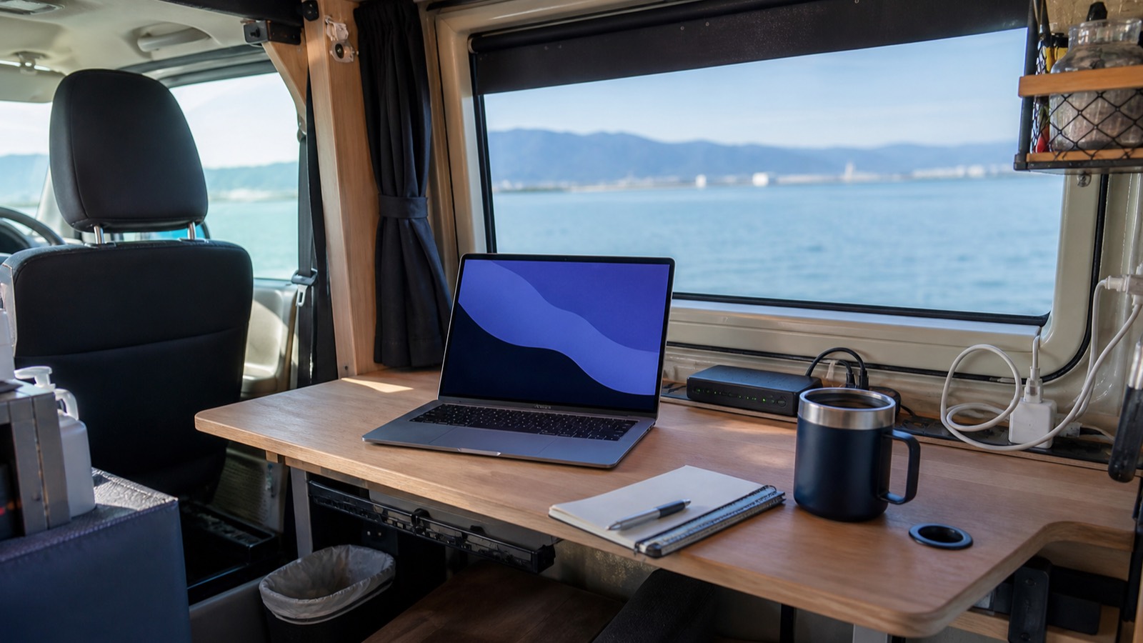 バン車内のノートPCと通信機器、飲み物を置いた仕事スペース（イメージ）