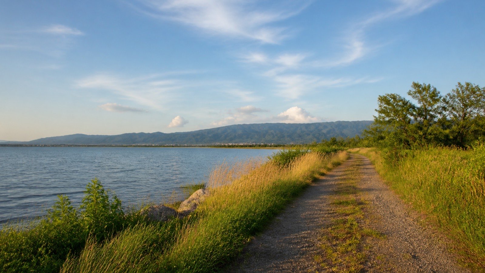 大きな湖と山を望む草辺の散歩道（イメージ）