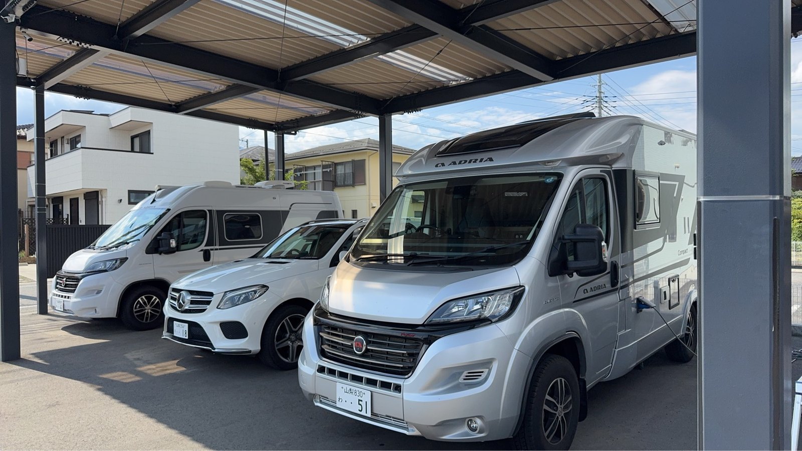 屋根付きスペースに並ぶADRIAなどのキャンピングカーと乗用車
