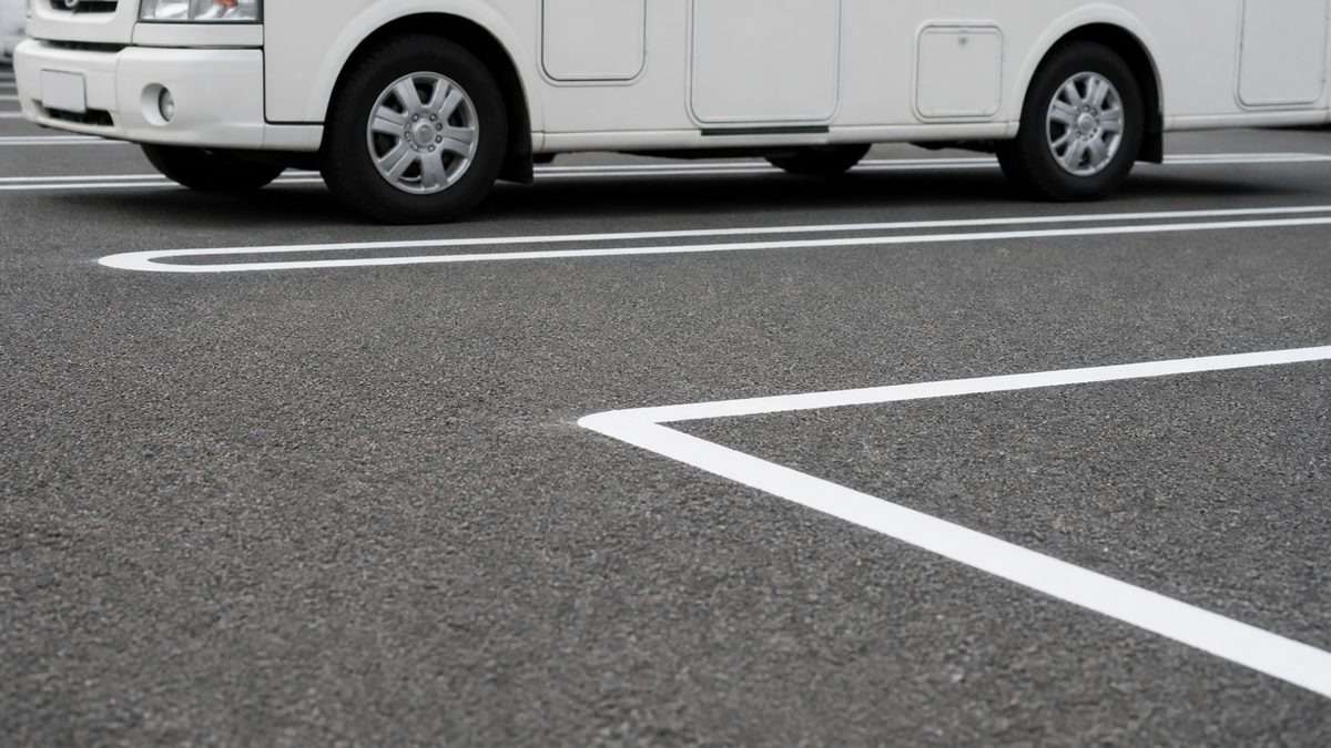 白い区画線で仕切られた空の駐車ますと、その奥に停まった白いキャンピングカーの側面