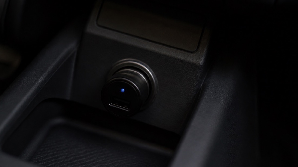 夜の車内。センターコンソールのシガーソケットに黒いUSB充電器がさし込まれ、小さな青いLEDが点いている