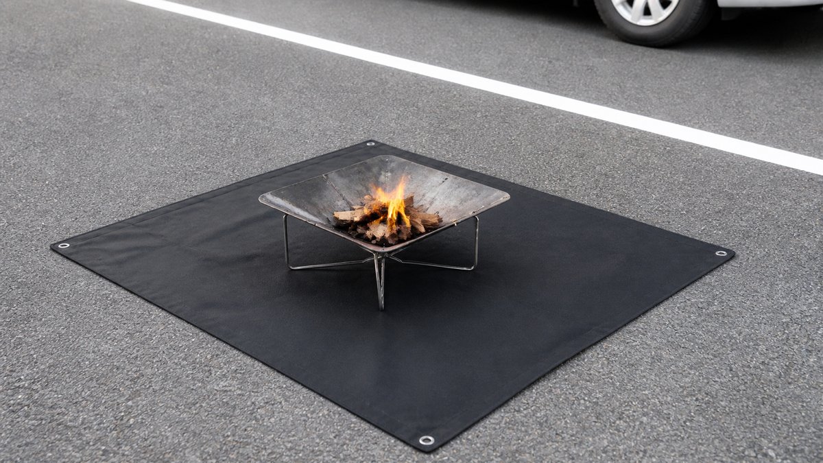 RVパークの駐車区画で、防火シートを敷いた上に置いた焚き火台に小さな炎が上がっている様子