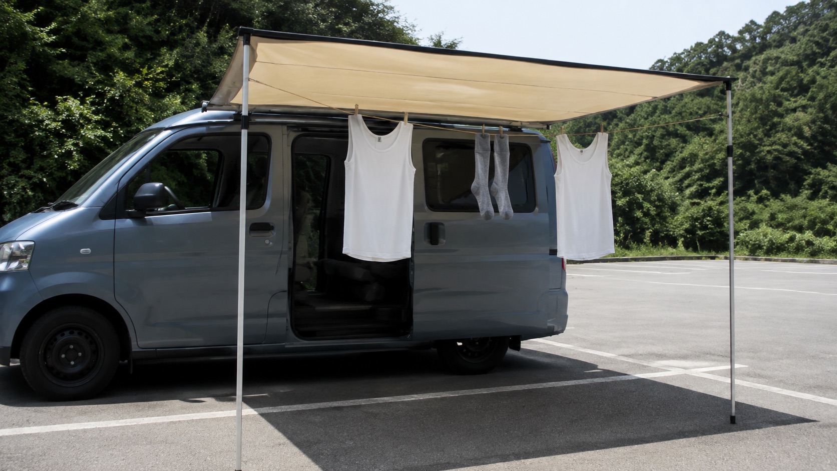 車の窓を開けた駐車スペースで、オーニングの下に張ったロープに肌着が数点だけ掛かっている昼の情景