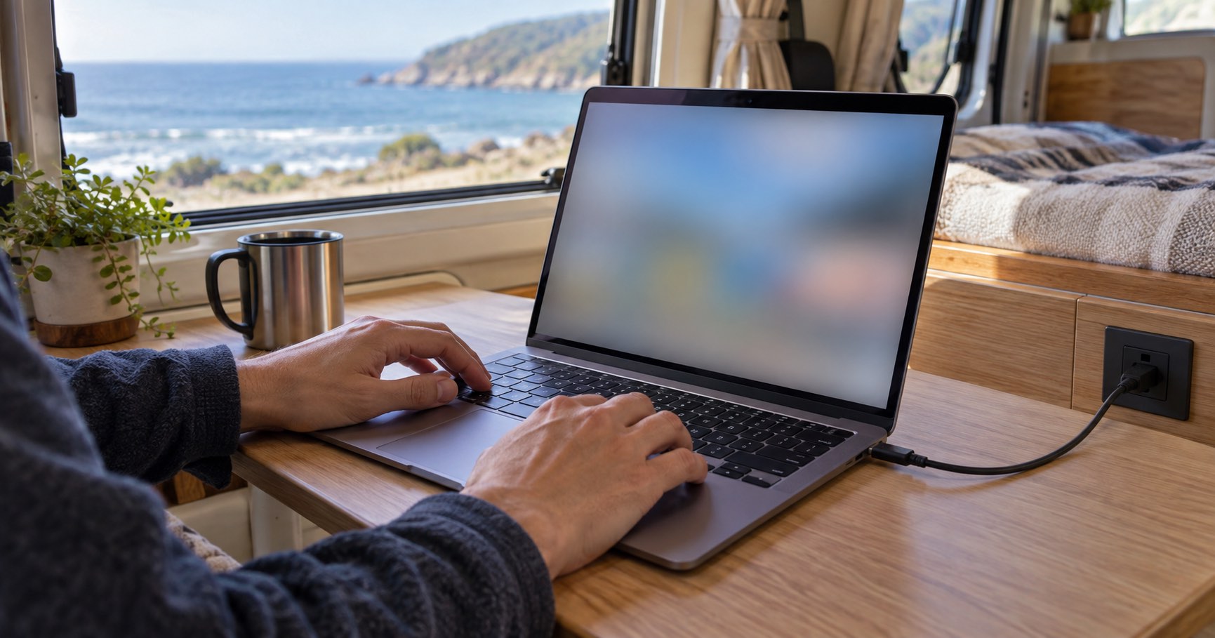 車内でノートPCを開く手元と、窓の外の海沿いの景色(イメージ)