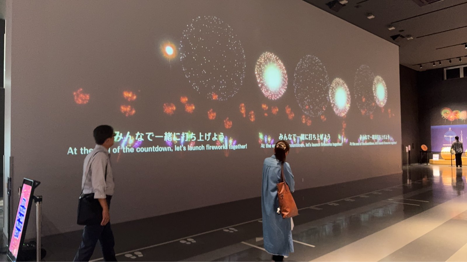 壁一面に投影された花火の映像を見上げる来館者