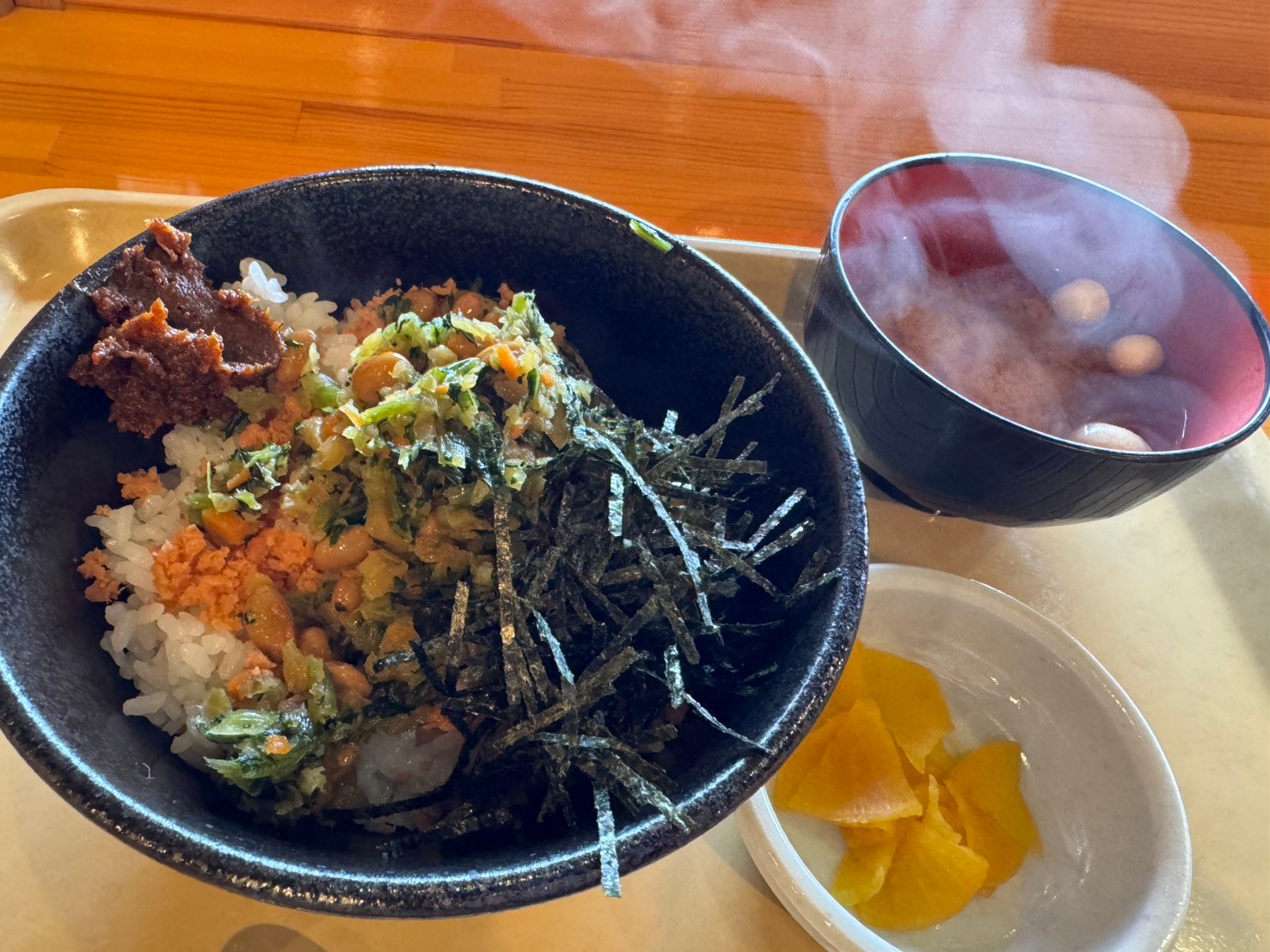 きりざい丼。ご飯に納豆、刻んだ菜っ葉の漬物、鮭、辛味噌、刻み海苔。湯気の立つ味噌汁とたくあん