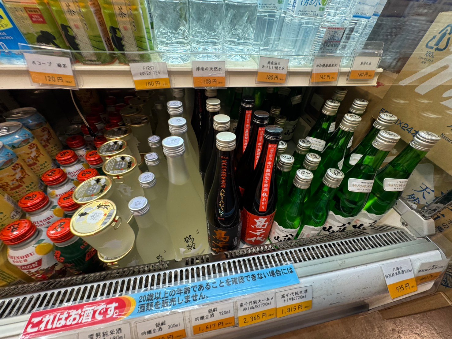 冷蔵ケースに並ぶ地酒。高千代、鶴齢、八海山などの銘柄と、南魚沼の湧き水のペットボトル