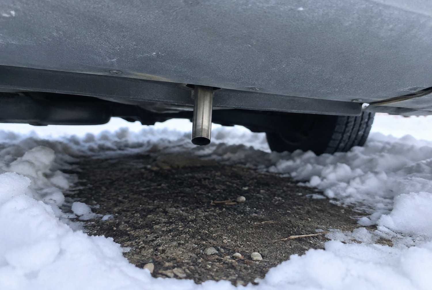 キャンピングカーの床下で、細いステンレスの排気管が真下を向いて車体からわずかに突き出し、周りの雪が取り除かれている様子（イメージ画像・AI生成。実際の車両・製品の写真ではありません）