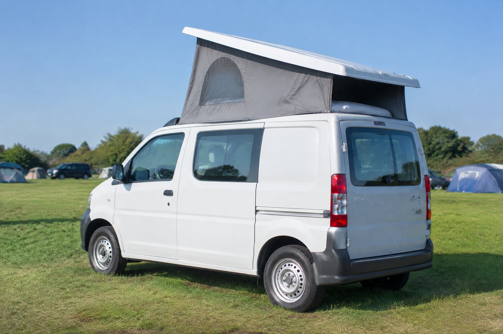 キャンプ場の芝生の横に停めた小型バンの屋根が持ち上がり、テント状の側面が見えている様子（イメージ画像・AI生成。実際の車両の写真ではありません）