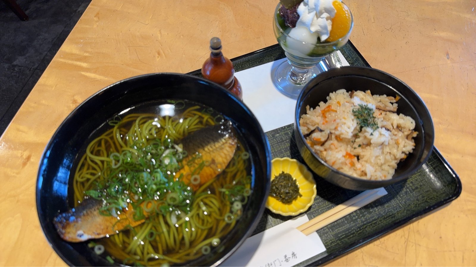 抹茶そばに大きなにしんをのせた一杯と、かやくご飯、ミニパフェ、黄色い小皿の佃煮