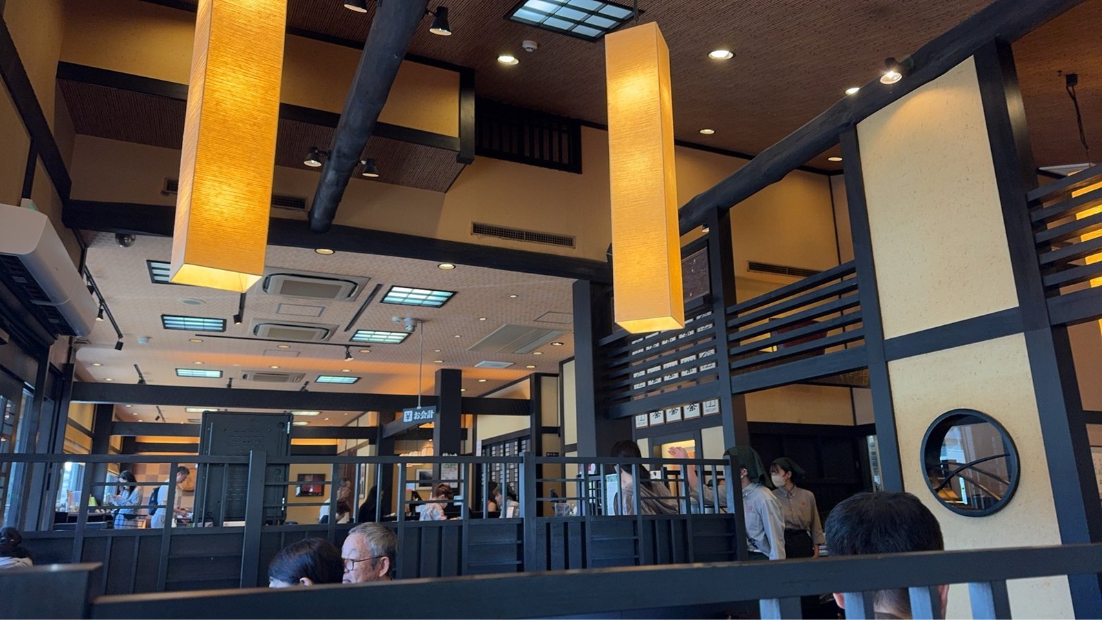 黒い梁と格子の仕切り、細長い照明、丸い窓が見える茶房の店内