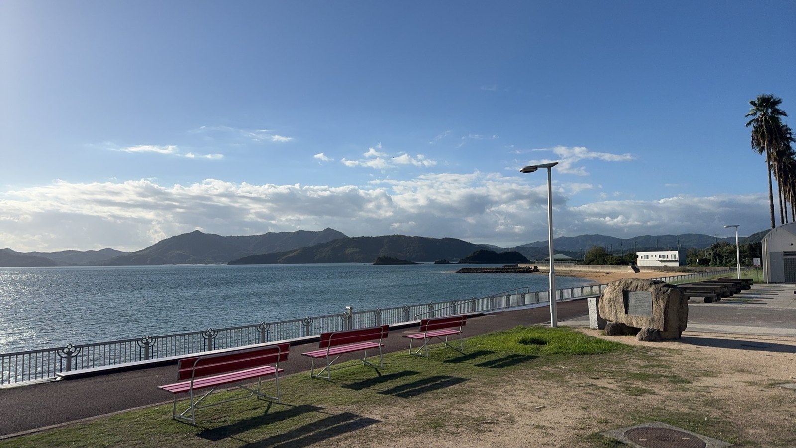 海沿いの赤いベンチと遊歩道、芝生、向こうに広がる海と島々