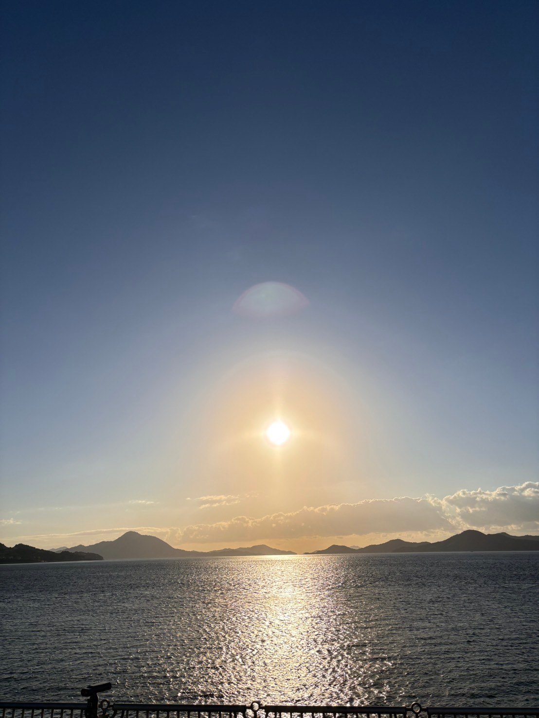 海の上の太陽と水面に反射する光、遠くに重なる島の輪郭