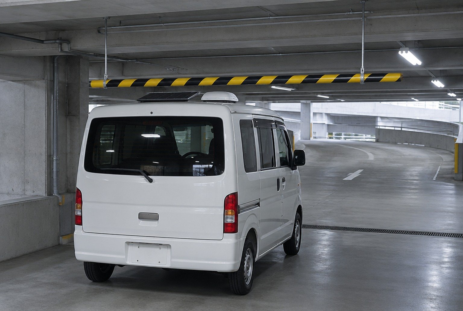 立体駐車場の入口の高さ制限バーの手前で止まった白い軽バン。屋根の上に薄いソーラーパネルが載っている（イメージ画像（AI生成。実際の施設・商品の写真ではありません））