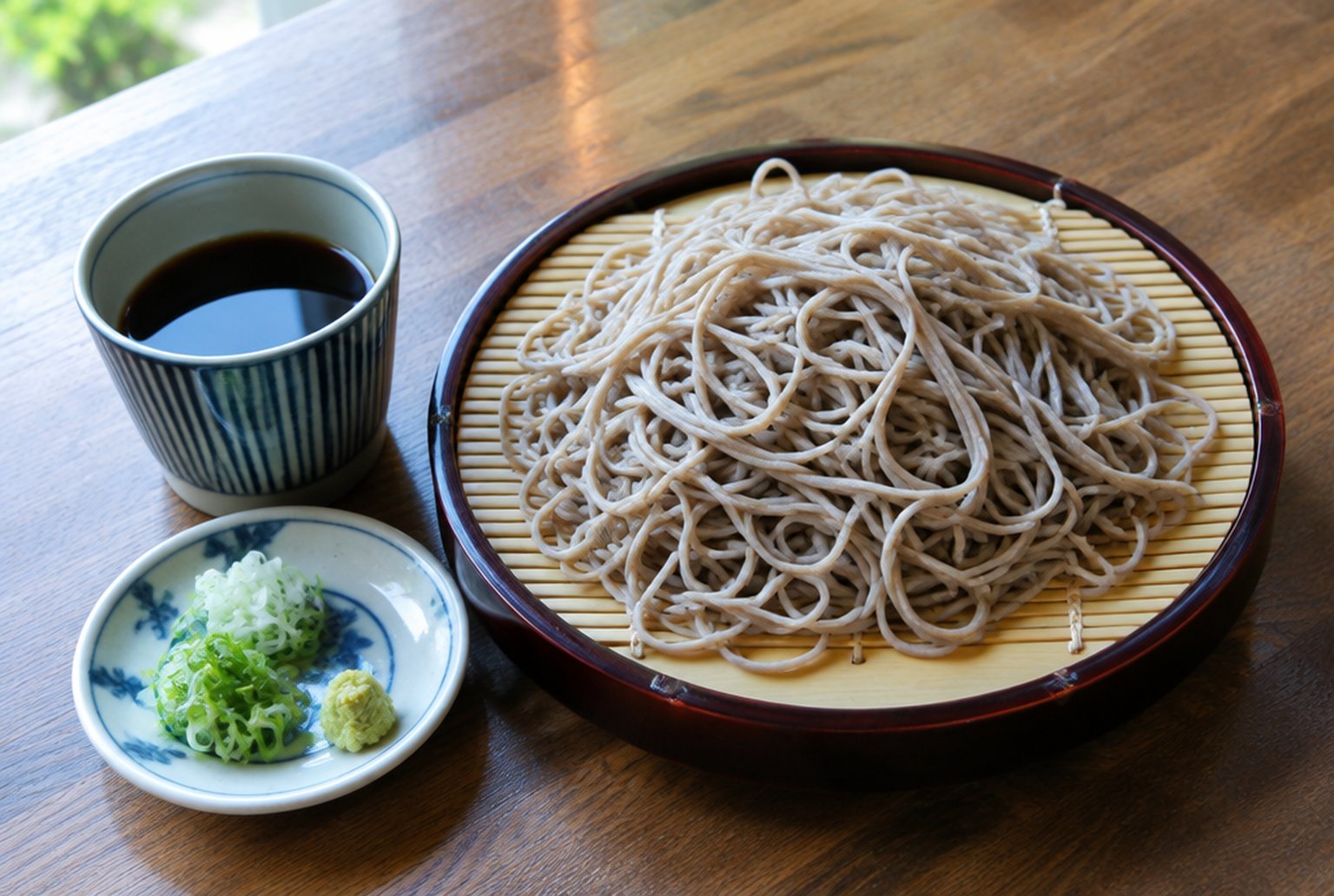 木のテーブルに置かれた竹のざるに盛ったもりそばと、そば猪口、小皿の薬味