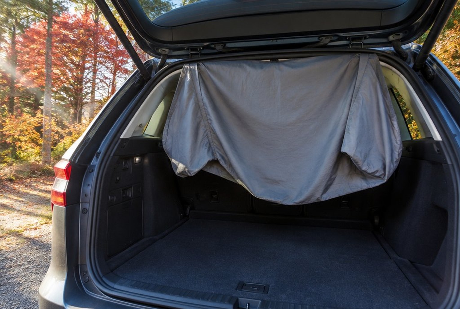 車のリアゲートを開けた荷室の上部に、グレーの無地のインナーシュラフが裏返してかけられ、朝の光で干されている。外には紅葉した木。イメージ画像（AI生成。実際の商品の写真ではありません）