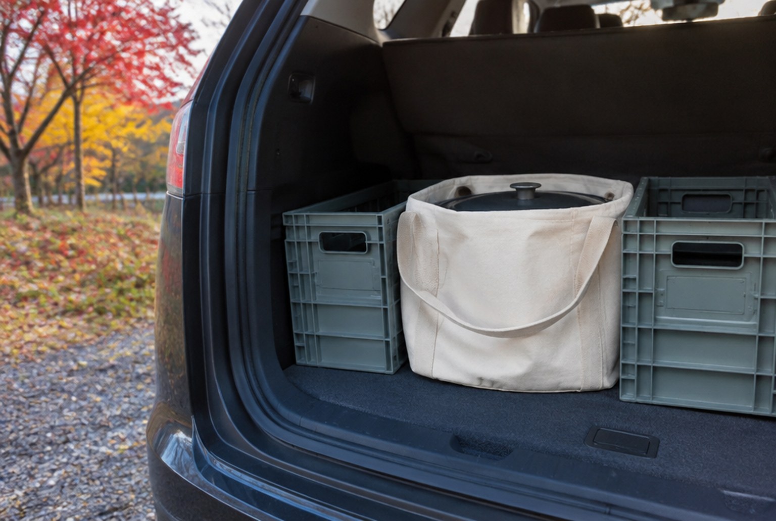 車のリアゲートを開けた荷室の床に、帆布の収納袋に入った丸いダッチオーブンが置かれ、横に折りたたみコンテナが並んでいる。外は紅葉した木と朝の光。イメージ画像（AI生成。実際の施設・商品の写真ではありません）