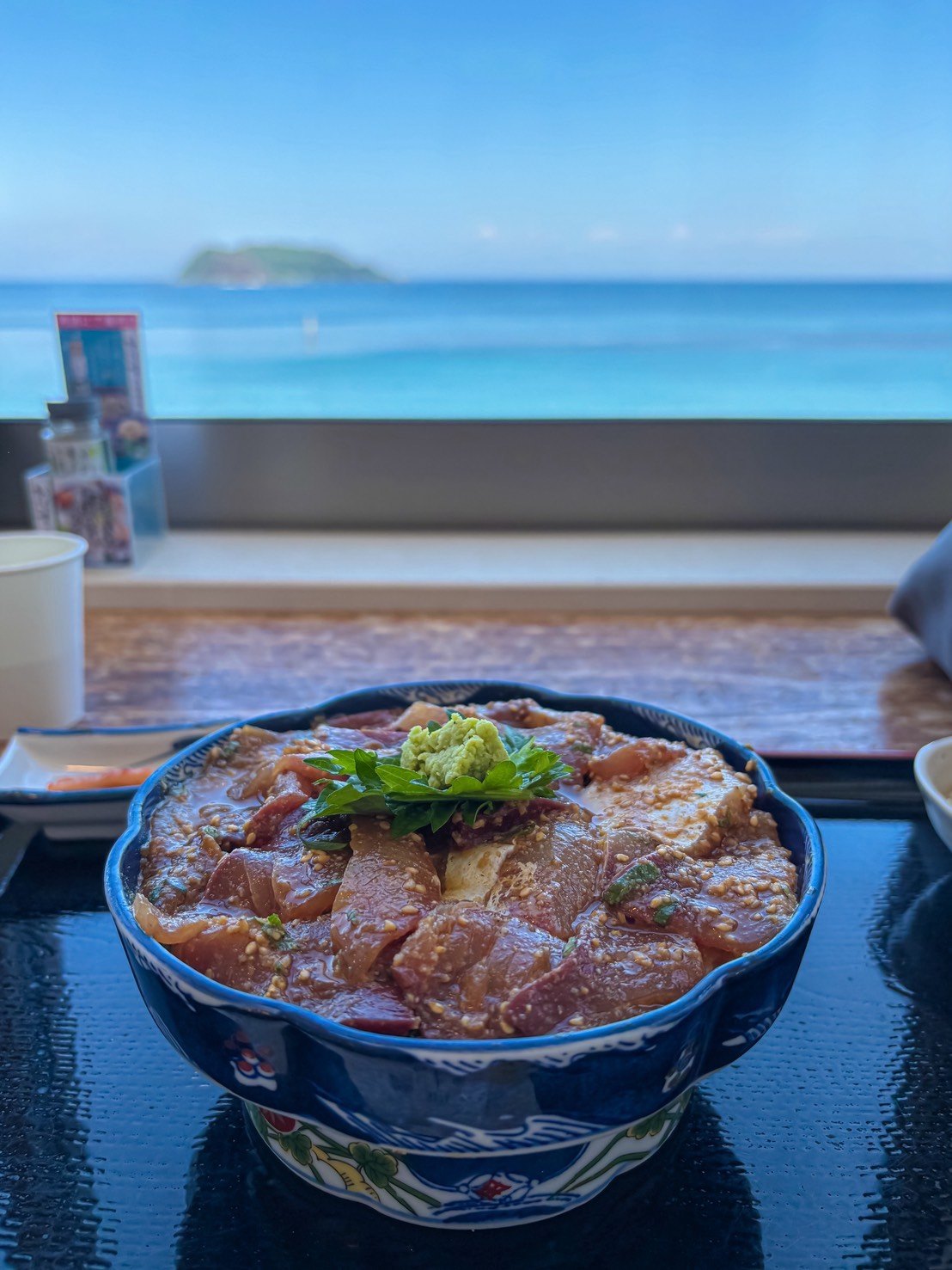 海の見える窓際に置かれた、ごまと大葉、わさびをのせた魚の丼