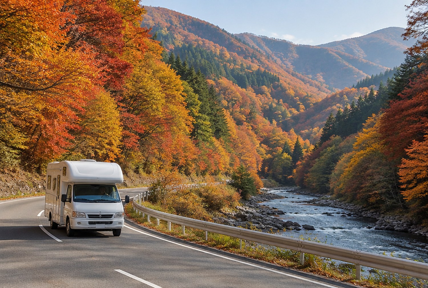 紅葉した山あいの谷を縫う二車線の道を、白いキャブコンが走っている。道の脇に川が流れ、斜面のカエデが赤や橙に色づいている（イメージ画像（AI生成。実際の施設・商品の写真ではありません））
