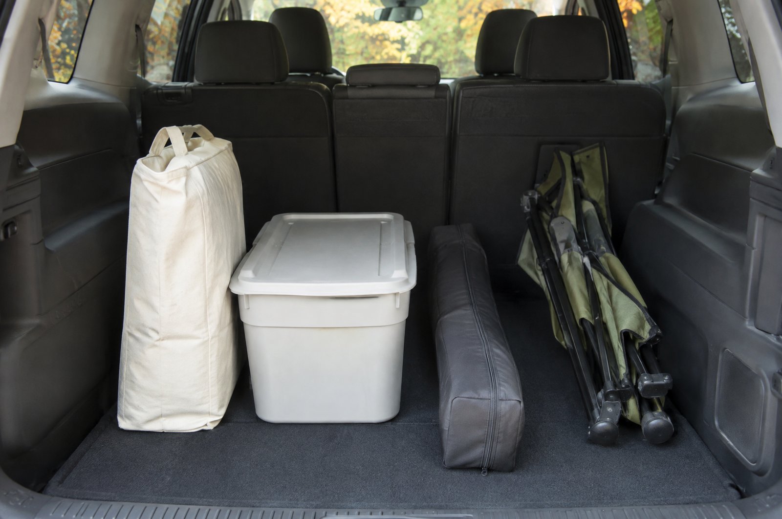 秋の朝、ミニバンの開いたリアゲートの荷室に、生成り色の布の収納袋が立ててあり、コンテナボックスの横に黒い細長い収納ケースが床に寝かせてある。イメージ画像(AI生成。実際の施設・商品の写真ではありません)